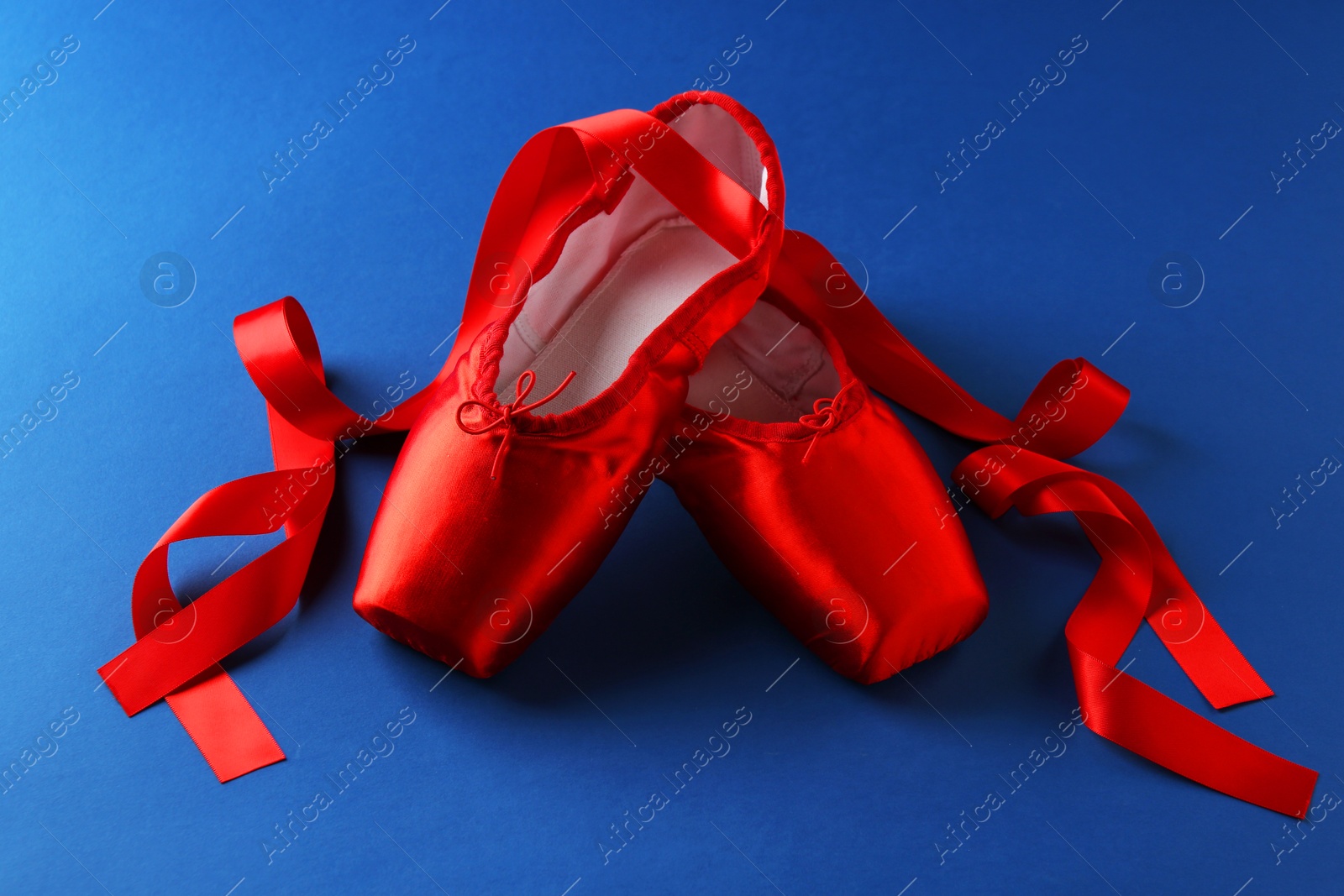 Photo of Pair of beautiful red pointe shoes on blue background