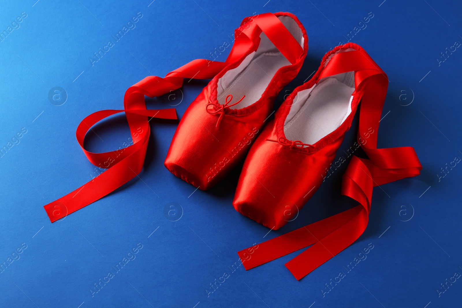 Photo of Pair of beautiful red pointe shoes on blue background