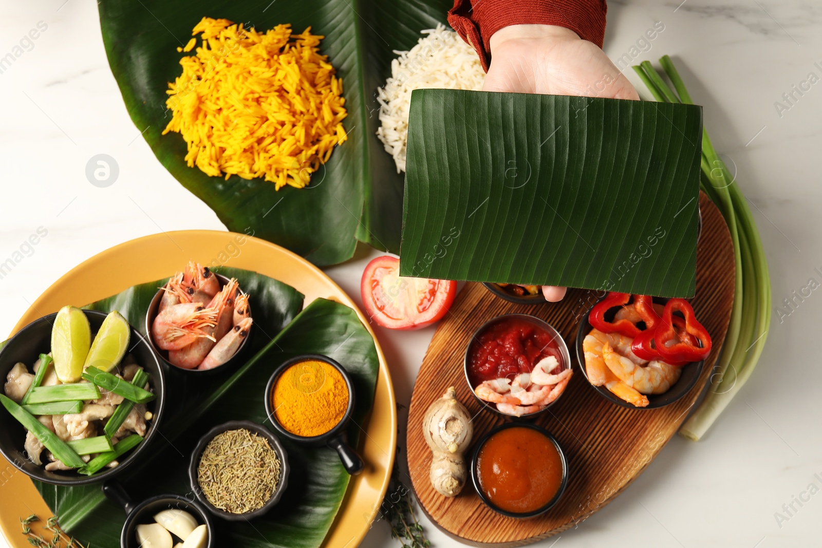 Photo of Woman holding piece of banana leaf at white table with tasty food, top view. Healthy eco serving