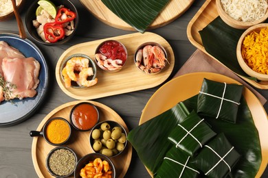 Photo of Different food wrapped in banana leaves, products, sauce and spices on wooden table, flat lay