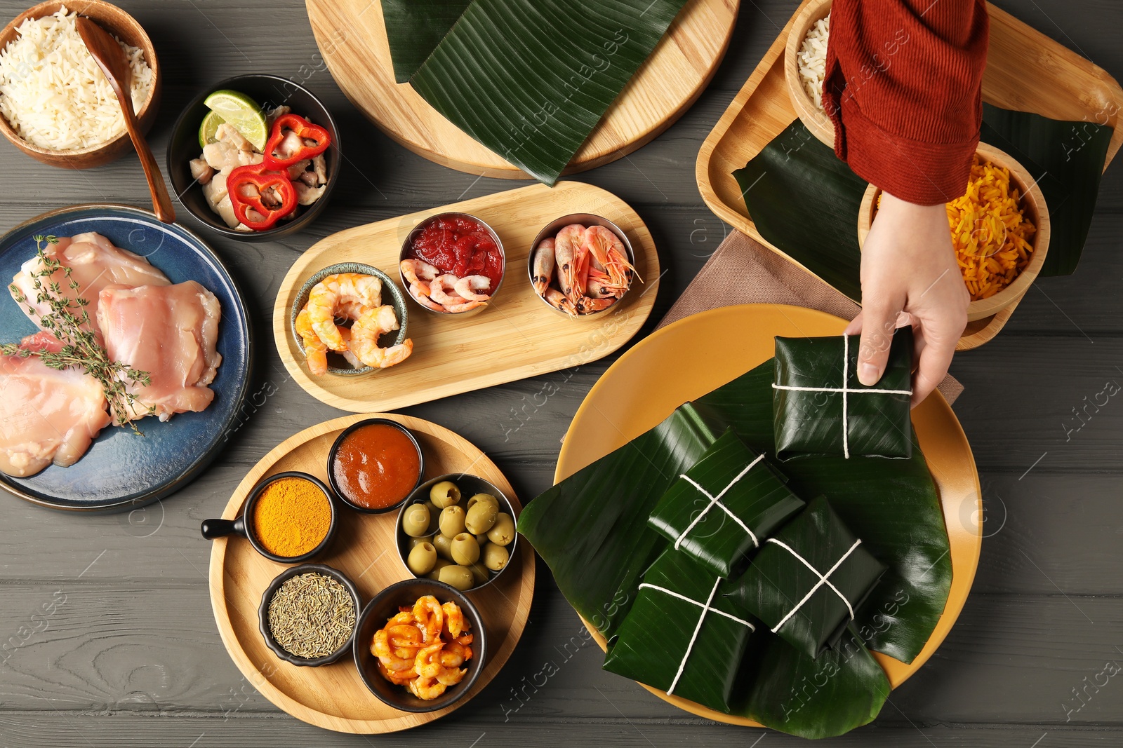 Photo of Woman taking folded banana leaf with food at wooden table with products, top view