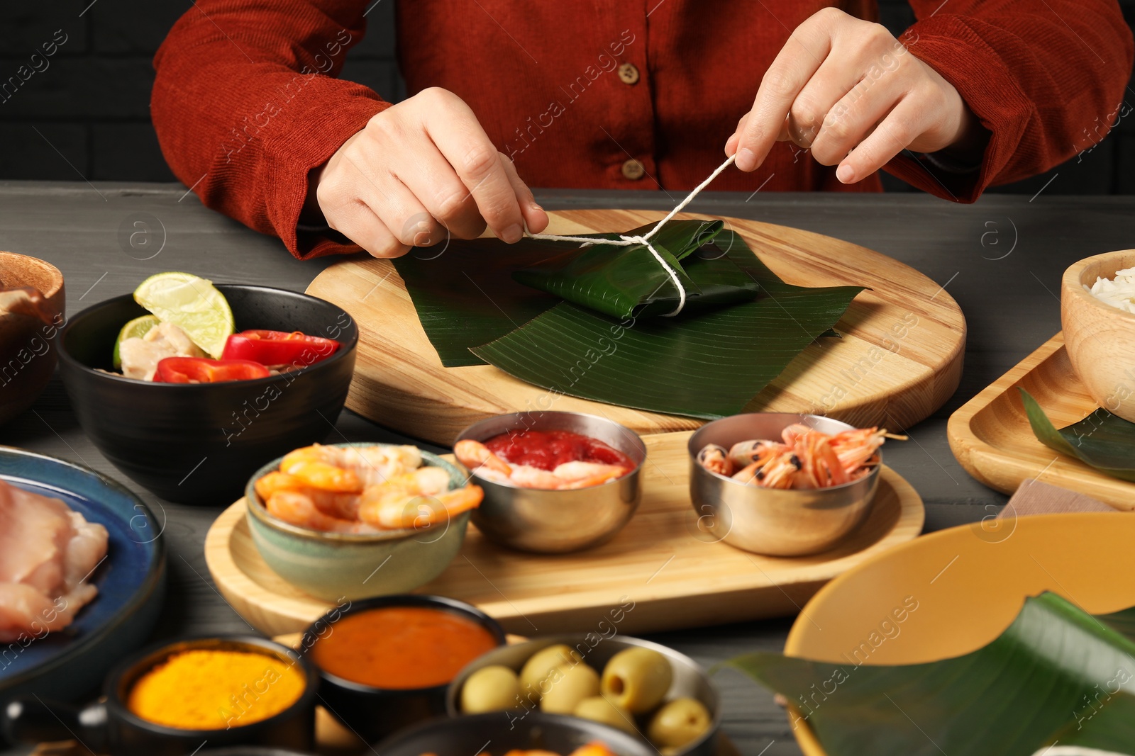 Photo of Woman tying banana leaf with food at wooden table with products, closeup. Healthy eco serving