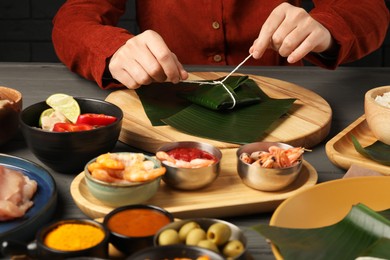 Photo of Woman tying banana leaf with food at wooden table with products, closeup. Healthy eco serving