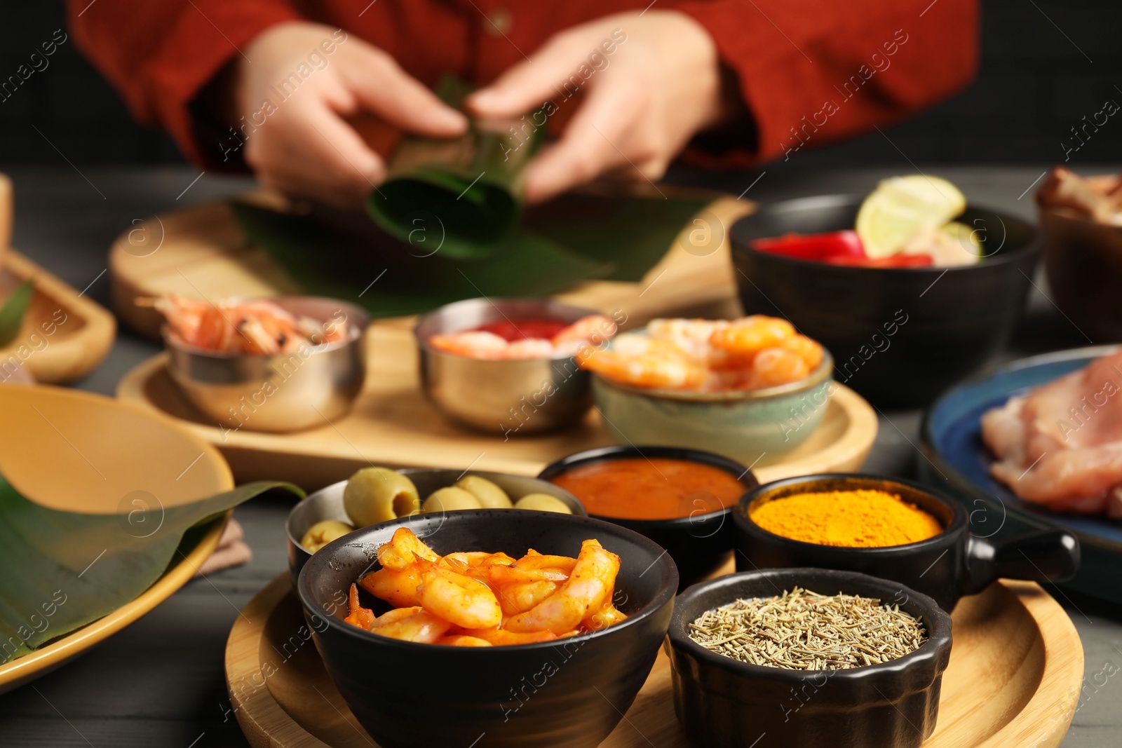 Photo of Woman wrapping food into banana leaf at wooden table with products, selective focus