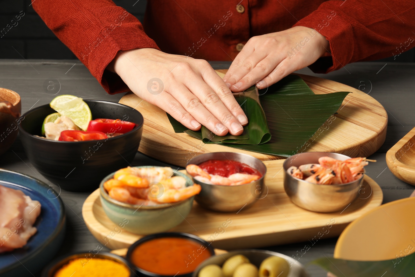 Photo of Woman wrapping food into banana leaf at wooden table with products, closeup. Healthy eco serving