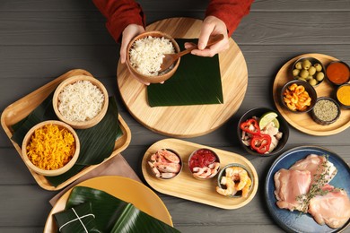 Photo of Woman putting rice onto banana leaf at wooden table with products, top view