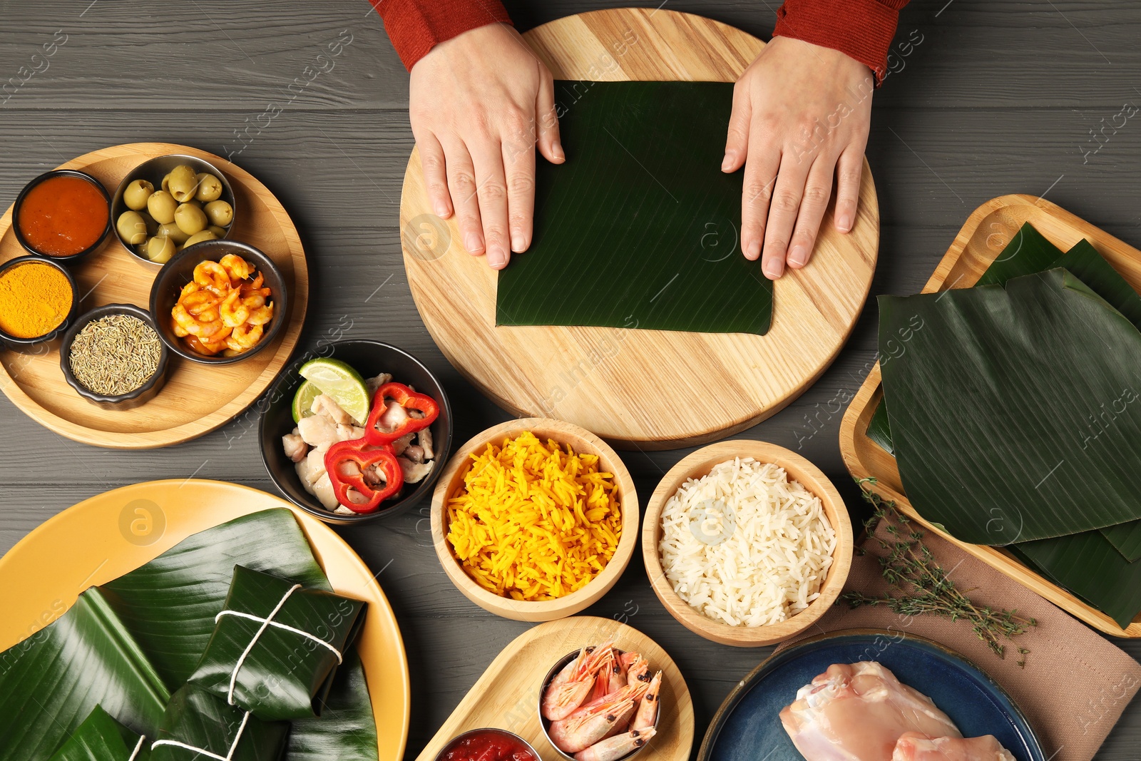 Photo of Woman with banana leaf at wooden table with different products, sauce and spices, top view. Healthy eco serving