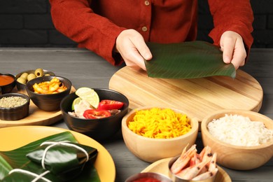 Photo of Woman with banana leaf at wooden table with different products, closeup. Healthy eco serving