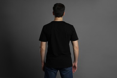 Photo of Man in blank black t-shirt on grey background, back view. Mockup for design