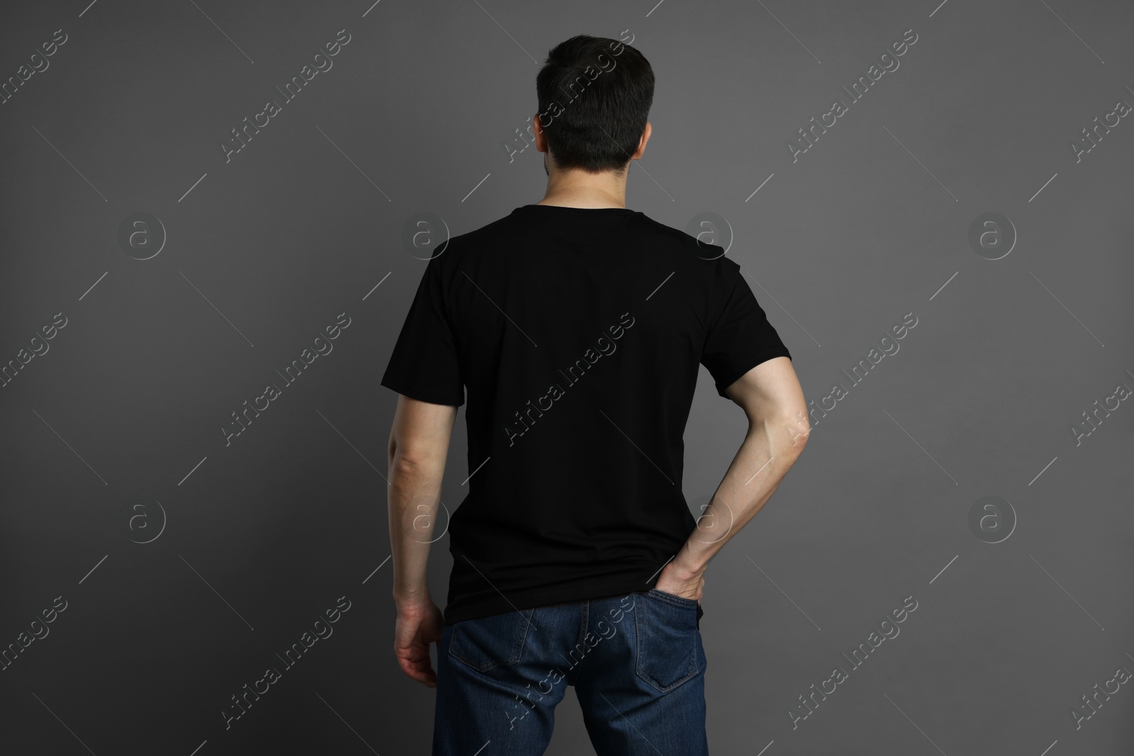 Photo of Man in blank black t-shirt on grey background, back view. Mockup for design