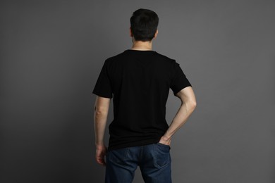 Photo of Man in blank black t-shirt on grey background, back view. Mockup for design