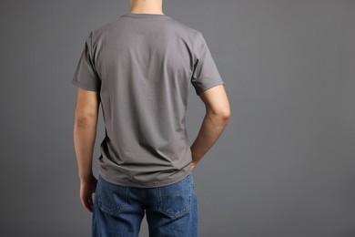 Photo of Man in stylish t-shirt on grey background, back view. Mockup for design