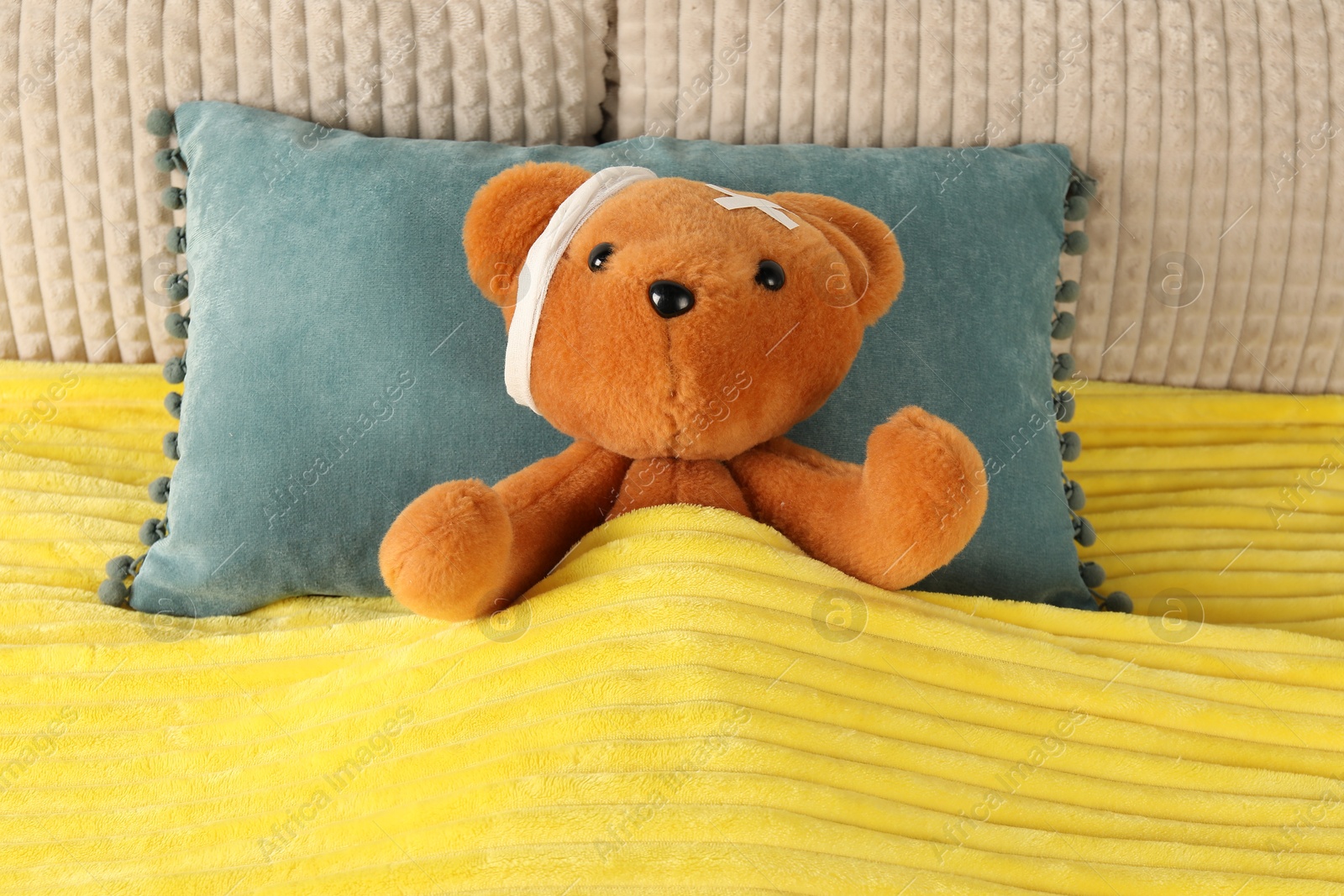 Photo of Cute teddy bear with bandage and adhesive medical plasters on bed, top view