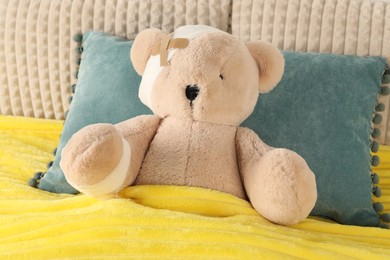 Photo of Cute teddy bear with bandages and adhesive medical plasters on bed