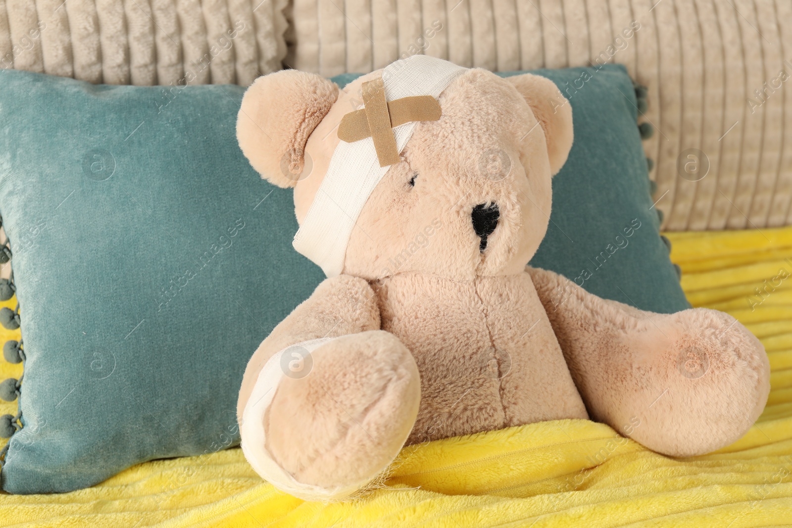 Photo of Cute teddy bear with bandages and adhesive medical plasters on bed