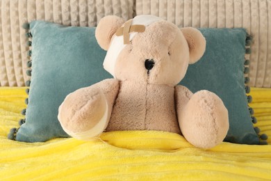 Photo of Cute teddy bear with bandages and adhesive medical plasters on bed, top view