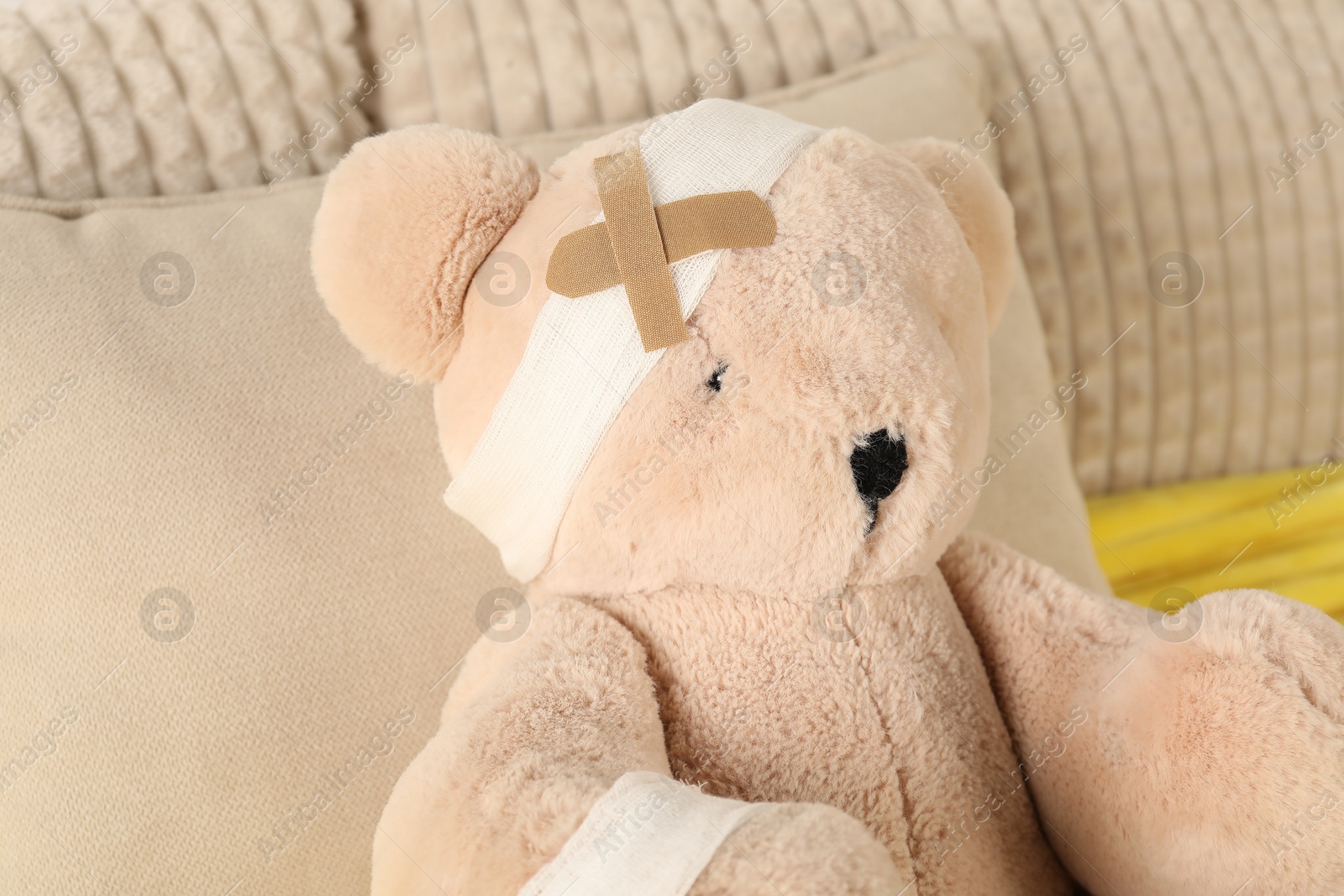 Photo of Cute teddy bear with bandages and adhesive medical plasters on bed