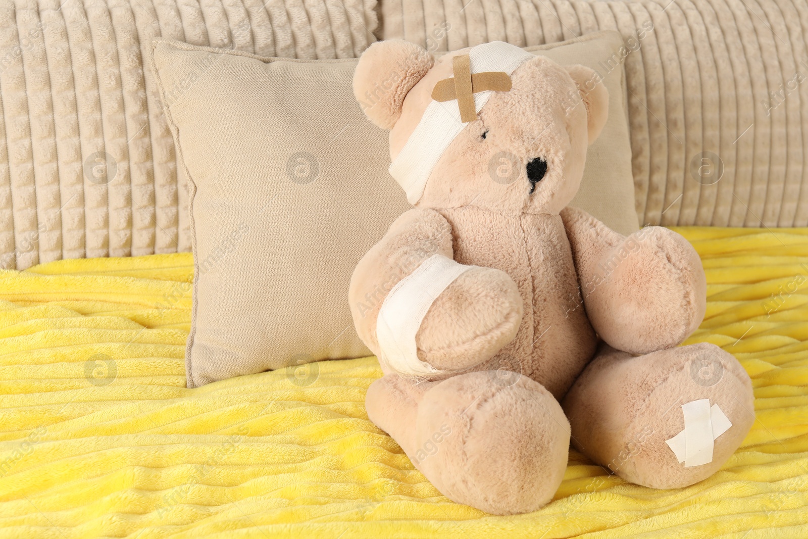 Photo of Cute teddy bear with bandages and adhesive medical plasters on bed