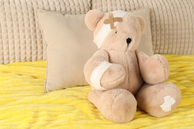 Photo of Cute teddy bear with bandages and adhesive medical plasters on bed