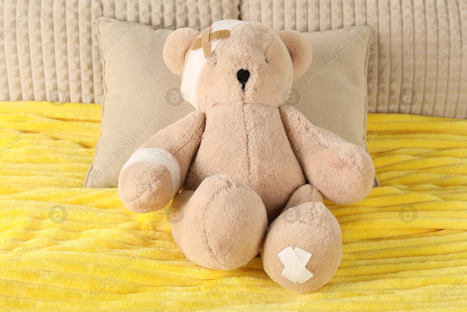 Photo of Cute teddy bear with bandages and adhesive medical plasters on bed