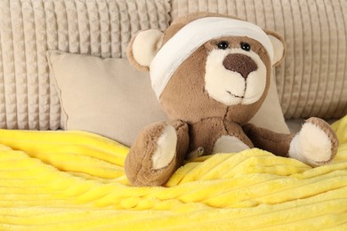 Photo of Cute teddy bear with bandages and thermometer on bed