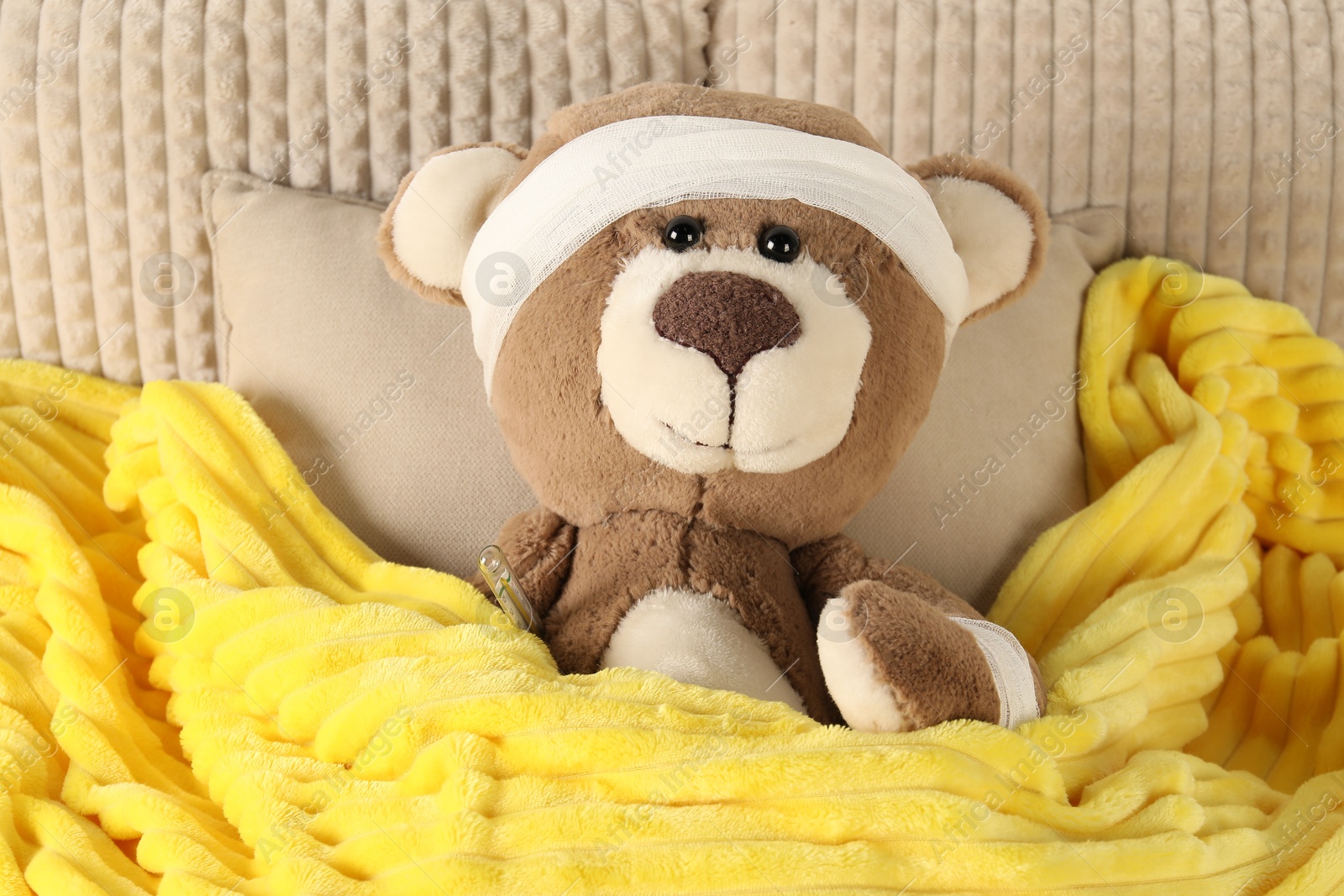 Photo of Cute teddy bear with bandages and thermometer on bed, top view