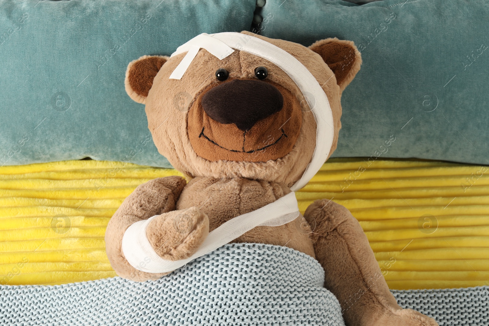 Photo of Cute teddy bear with bandages and adhesive medical plasters on bed, top view