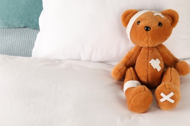 Photo of Cute teddy bear with bandages and adhesive medical plasters on bed, space for text