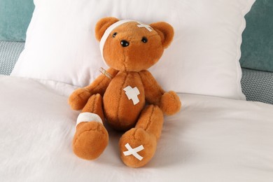 Photo of Cute teddy bear with bandages, adhesive medical plasters and thermometer on bed