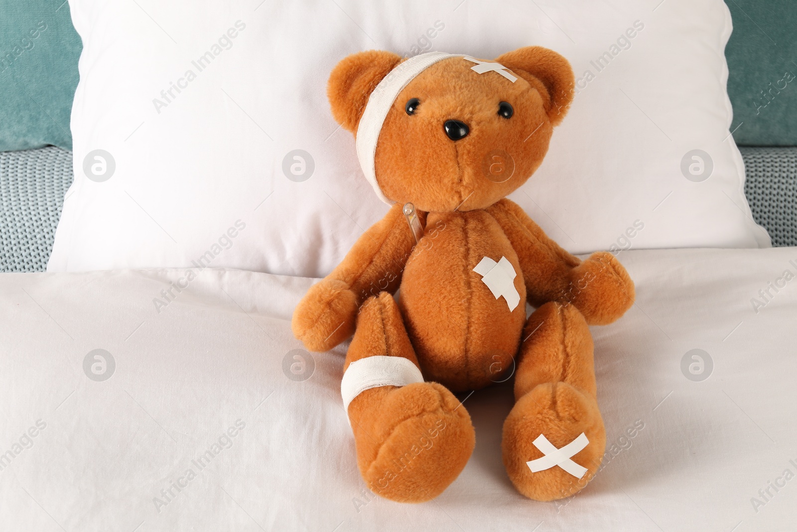 Photo of Cute teddy bear with bandages, adhesive medical plasters and thermometer on bed