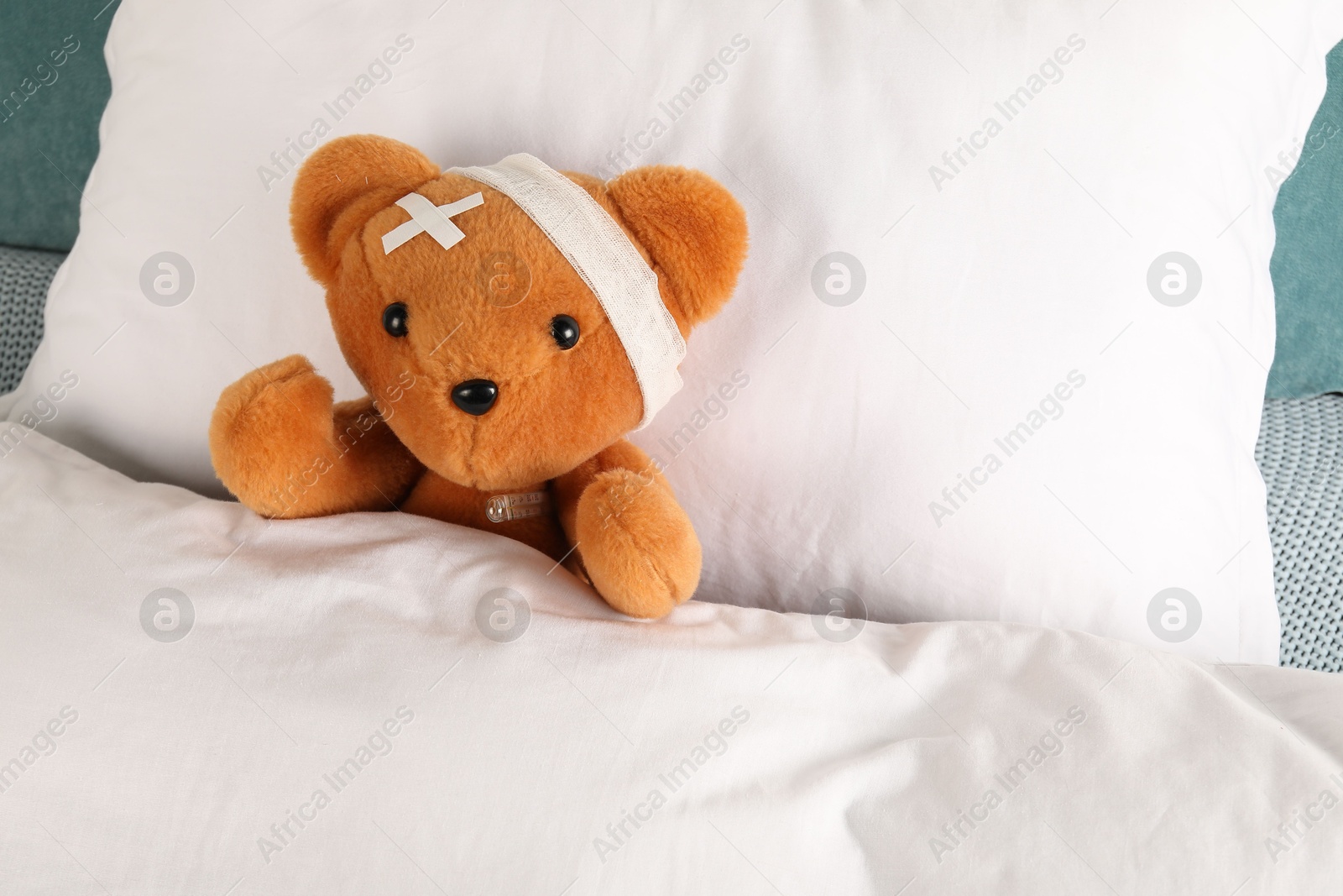 Photo of Cute teddy bear with bandage, adhesive medical plasters and thermometer on bed