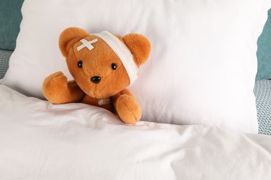 Photo of Cute teddy bear with bandage, adhesive medical plasters and thermometer on bed