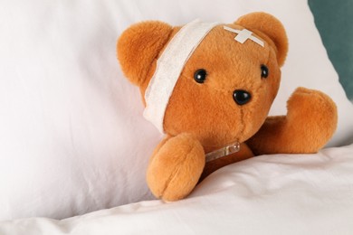 Photo of Cute teddy bear with bandage, adhesive medical plasters and thermometer on bed