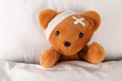 Photo of Cute teddy bear with bandage and adhesive medical plasters on bed, top view