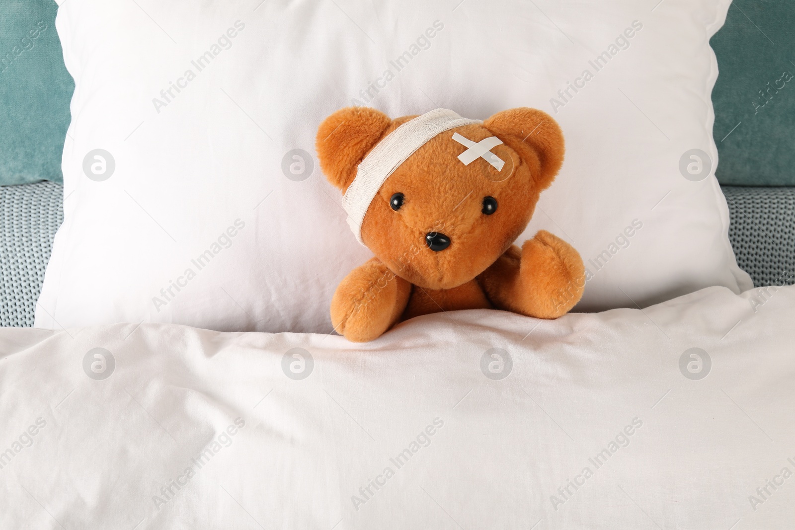 Photo of Cute teddy bear with bandage and adhesive medical plasters on bed, top view