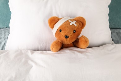 Photo of Cute teddy bear with bandage and adhesive medical plasters on bed, top view