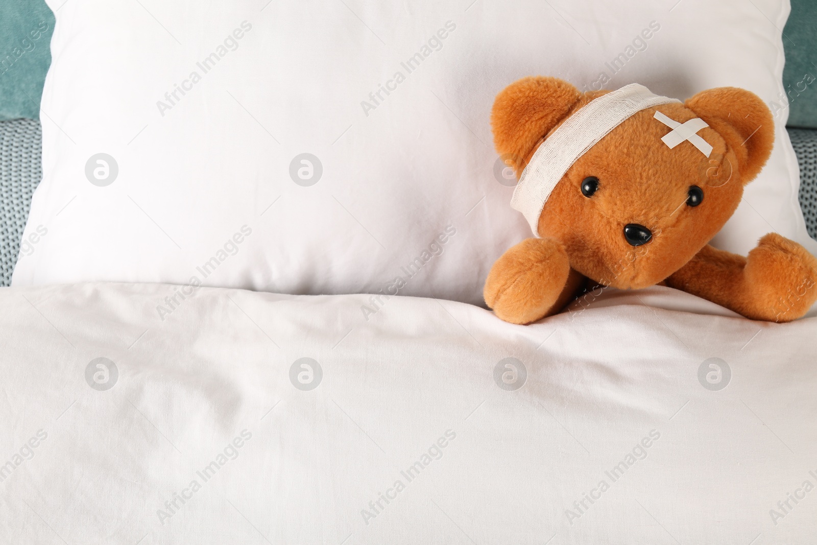 Photo of Cute teddy bear with bandage and adhesive medical plasters on bed, top view. Space for text