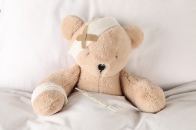 Photo of Cute teddy bear with bandages, adhesive medical plasters and thermometer on bed, top view