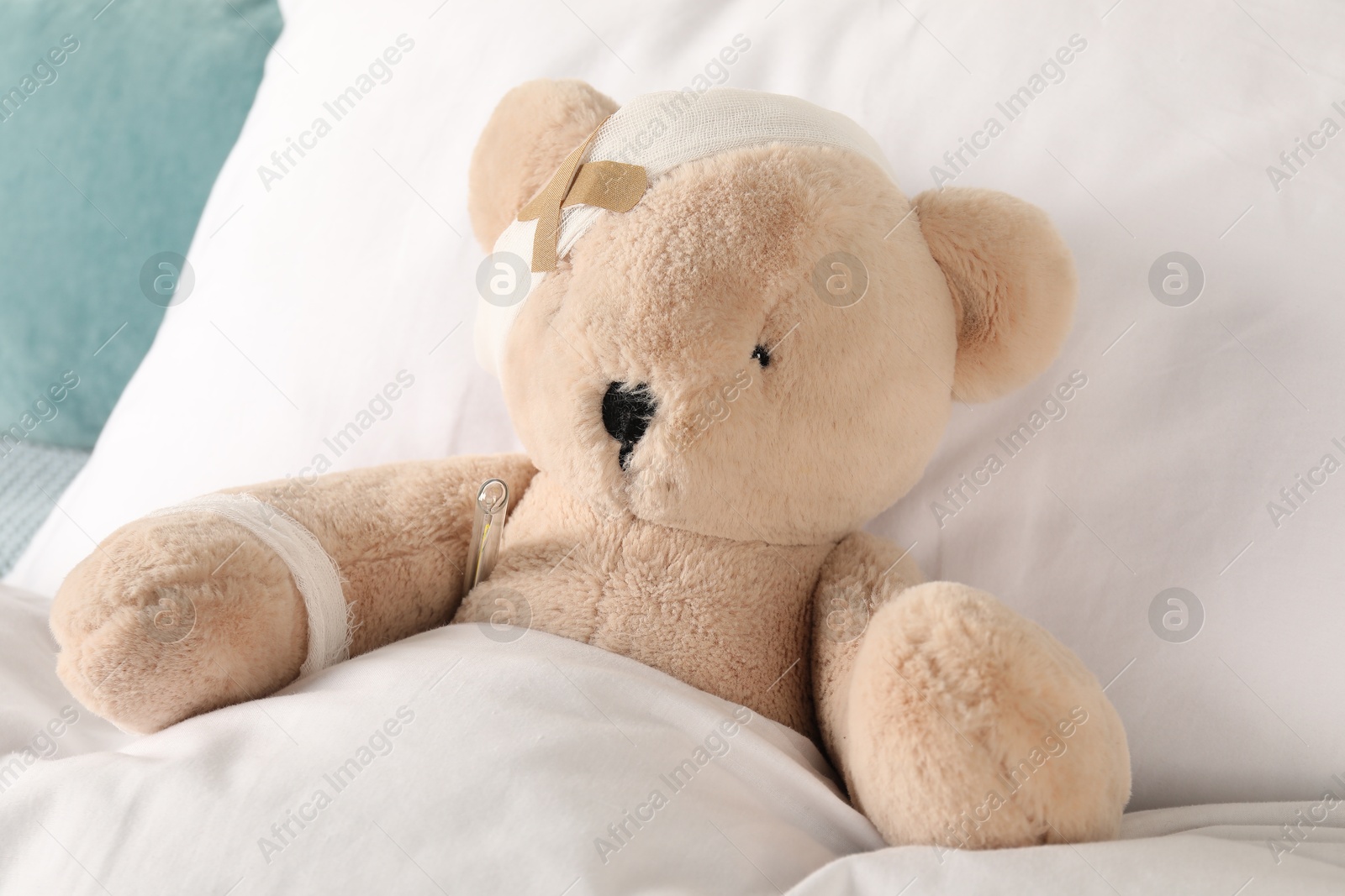 Photo of Cute teddy bear with bandages, adhesive medical plasters and thermometer on bed