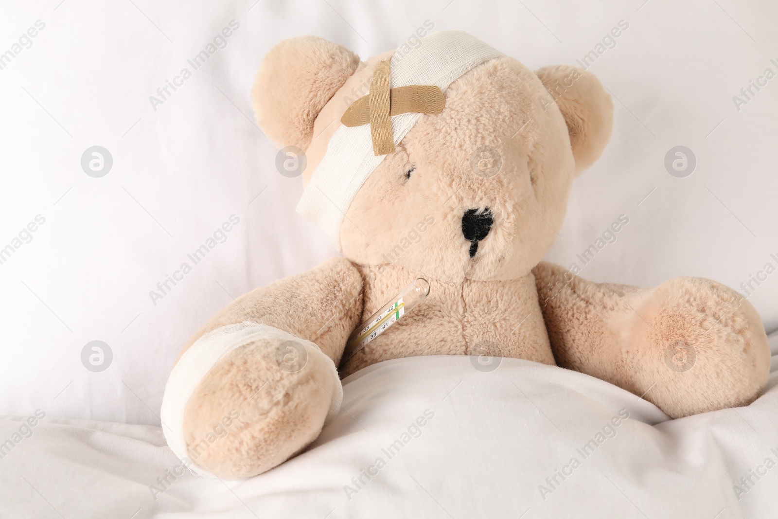 Photo of Cute teddy bear with bandages, adhesive medical plasters and thermometer on bed