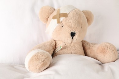 Photo of Cute teddy bear with bandages, adhesive medical plasters and thermometer on bed