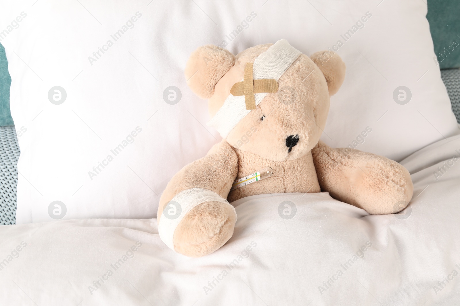 Photo of Cute teddy bear with bandages, adhesive medical plasters and thermometer on bed