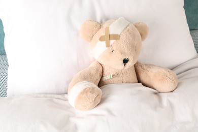 Photo of Cute teddy bear with bandages, adhesive medical plasters and thermometer on bed