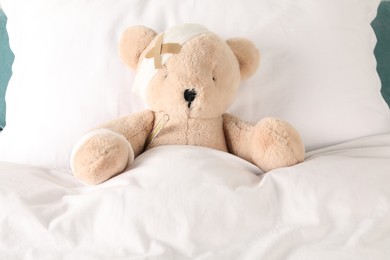 Photo of Cute teddy bear with bandages, adhesive medical plasters and thermometer on bed, top view