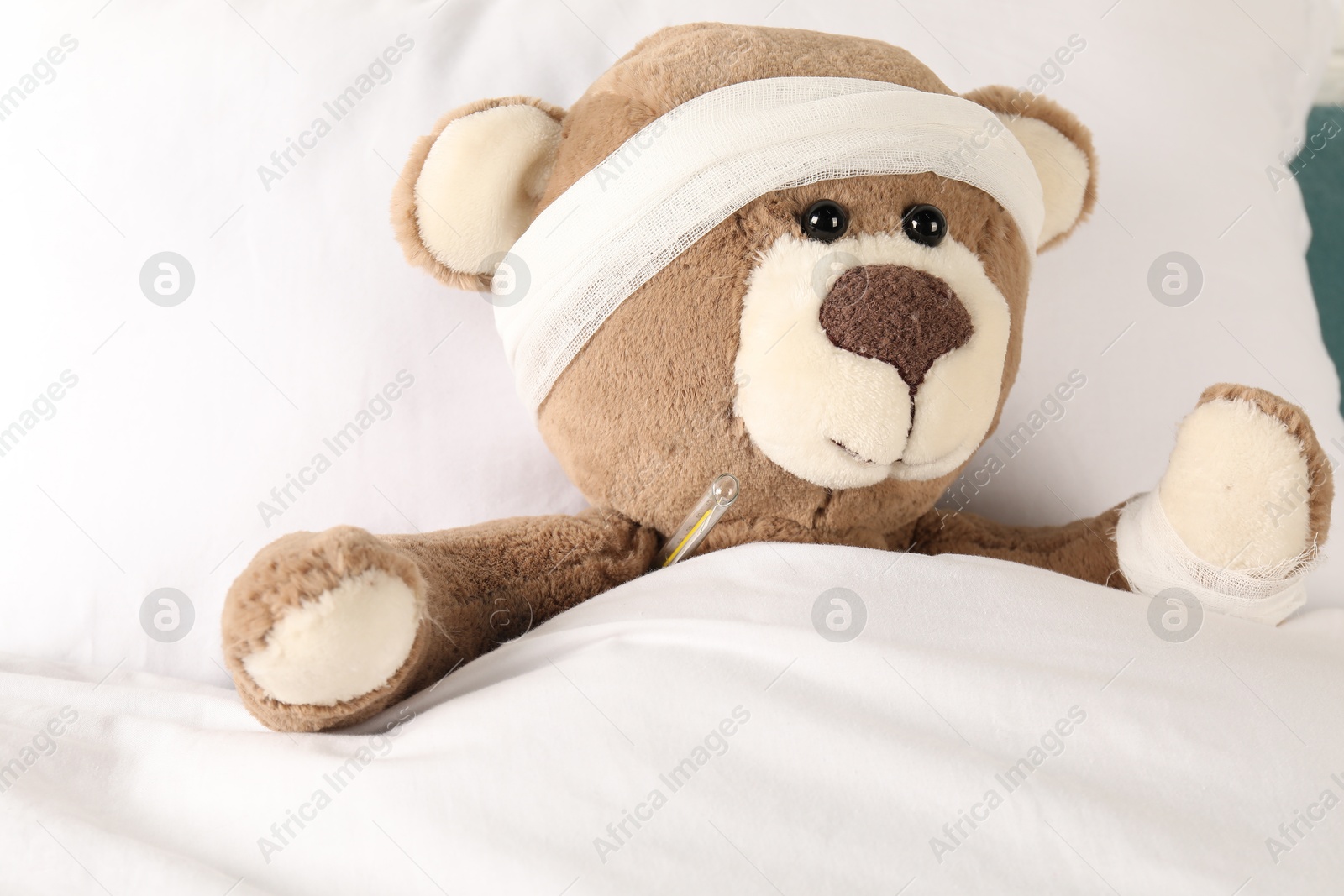 Photo of Cute teddy bear with bandages and thermometer on bed