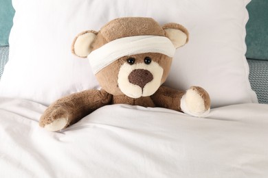 Photo of Cute teddy bear with bandages on bed, top view