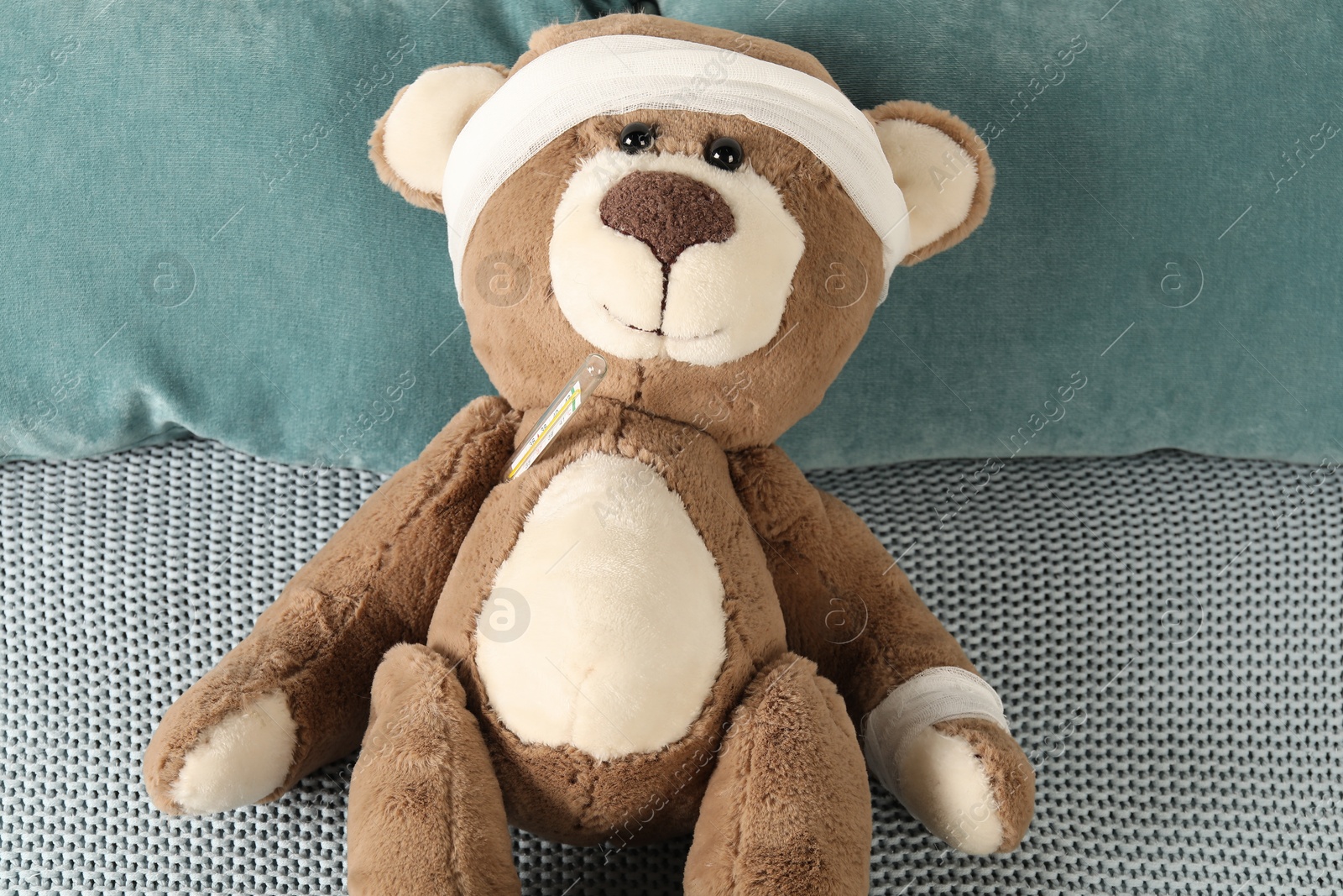 Photo of Cute teddy bear with bandages and thermometer on bed, top view