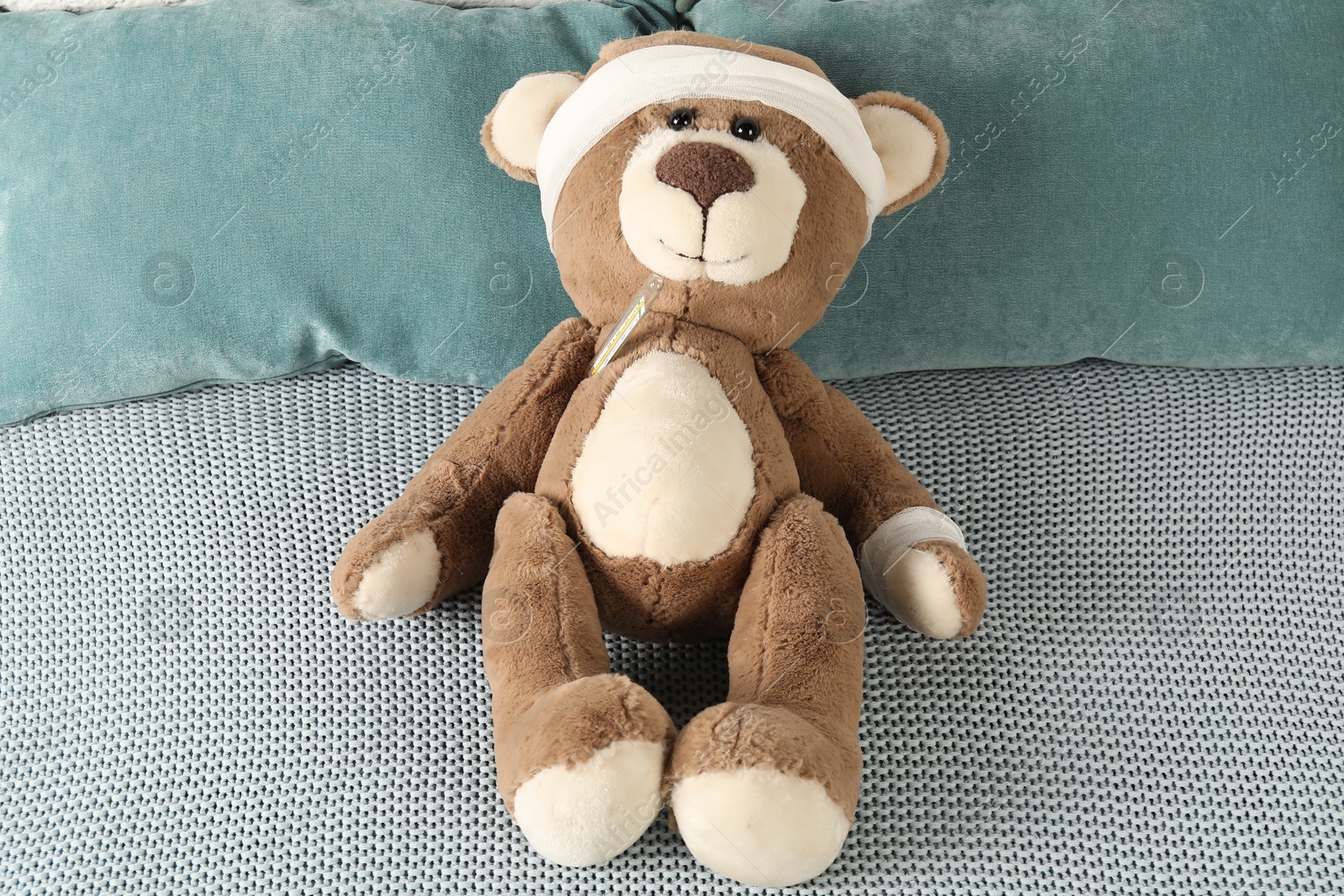 Photo of Cute teddy bear with bandages and thermometer on bed, top view