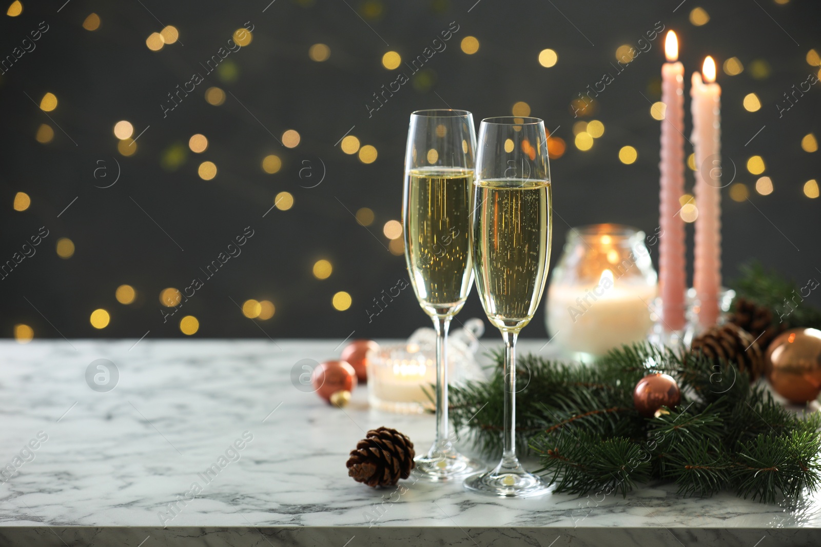 Photo of Delicious champagne in glasses and Christmas decor on marble table against blurred lights. Space for text