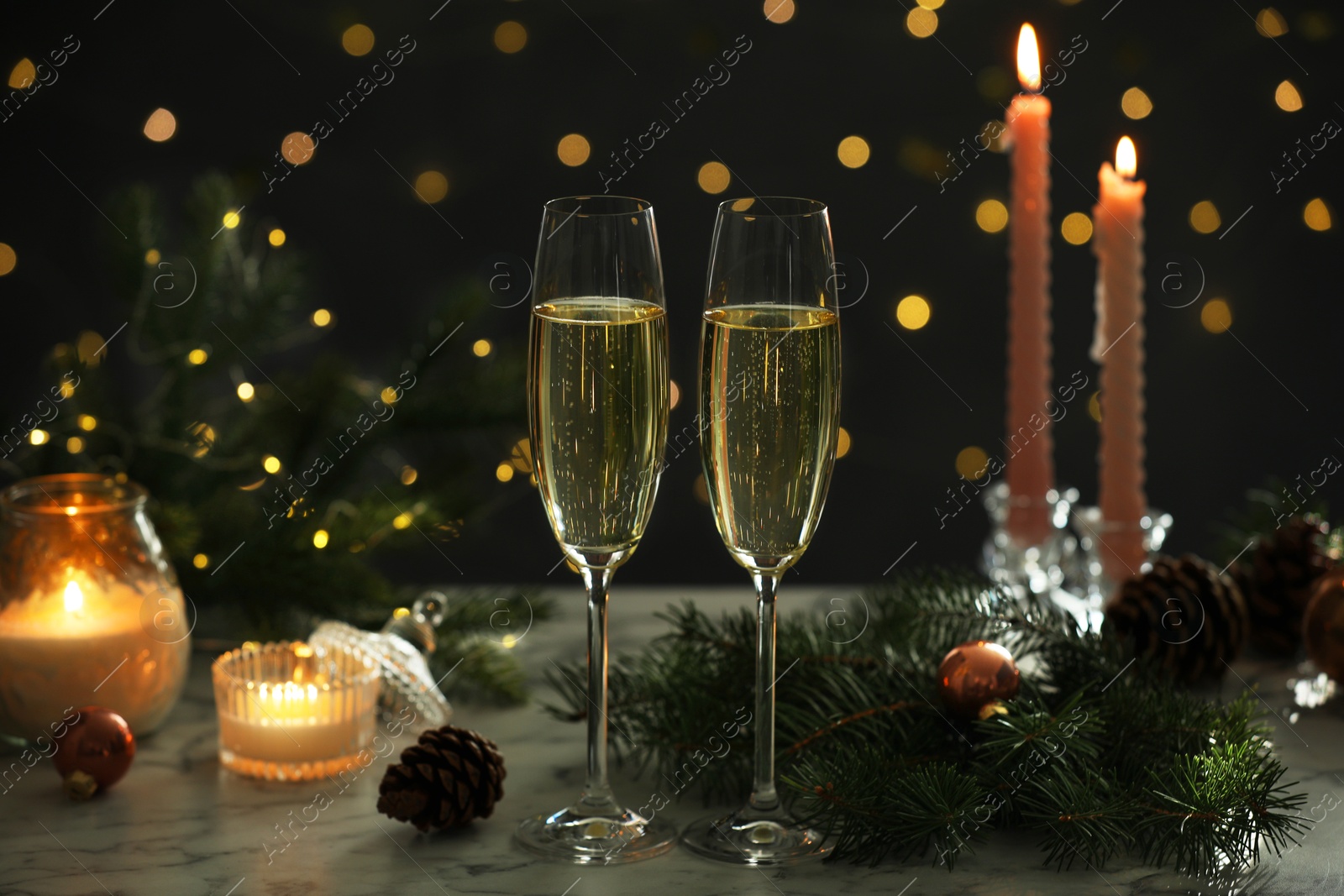 Photo of Delicious champagne in glasses and Christmas decor on marble table against blurred lights